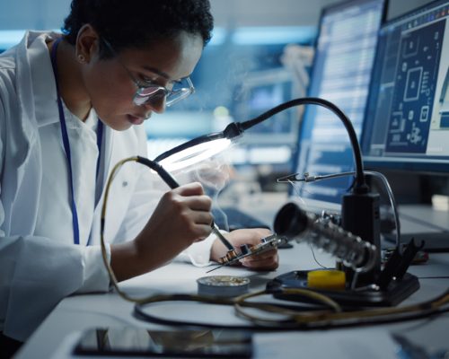 Modern Electronics Research, Development Facility: Black Female Engineer Does Computer Motherboard Soldering. Scientists Design PCB, Silicon Microchips, Semiconductors. Medium Close-up Shot